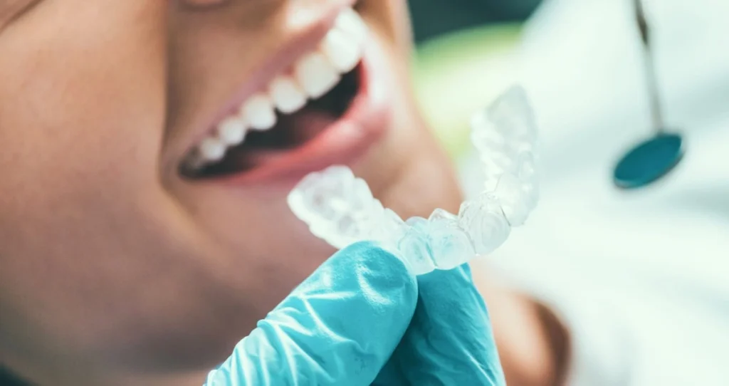 Dentist wearing gloves holding clear aligners in front of a smiling patient after successful orthodontic treatment